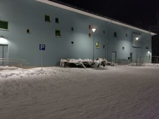 Kriivarin koulun parkkipaikka talvi-iltana, siniharmaa seinä jossa P-kyltti