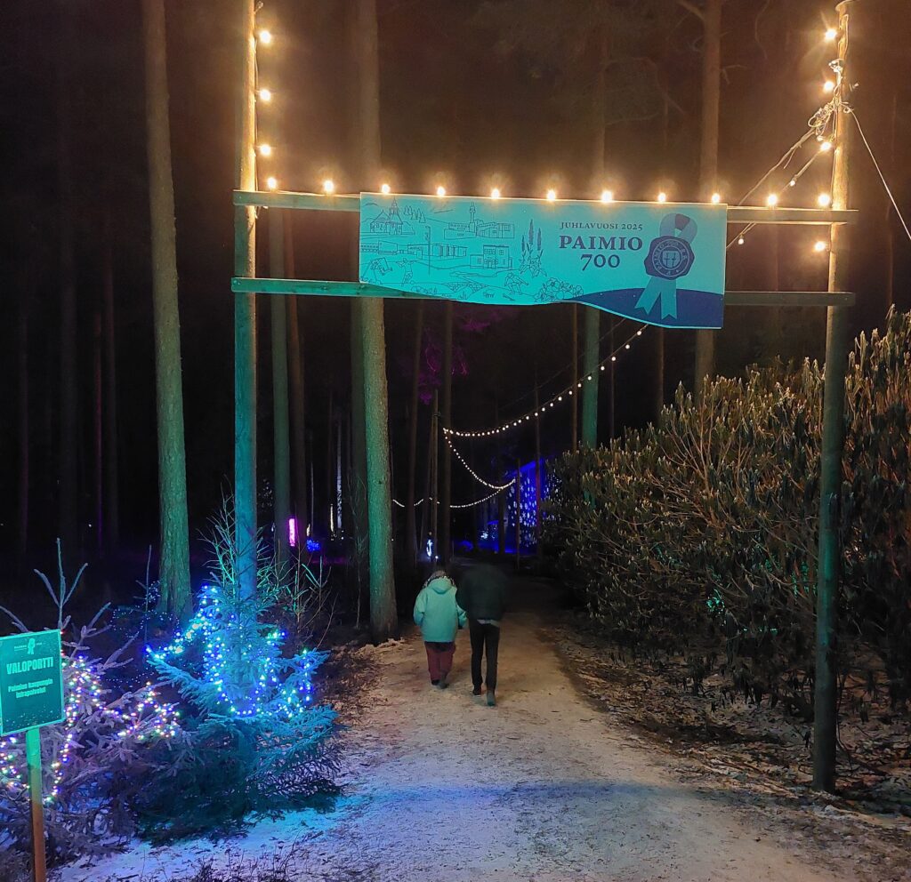 Valaistu, talvinen polku - yläpuolella Paimio 700 -juhlavuoden kyltti.