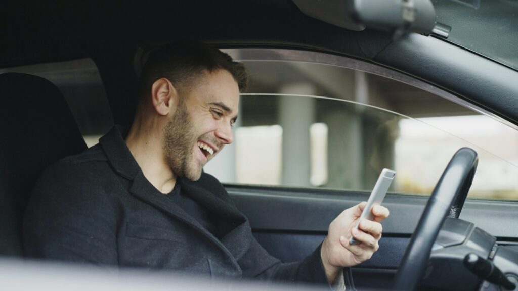 Henkilö katsoo puhelinta autossa sisällä istuen