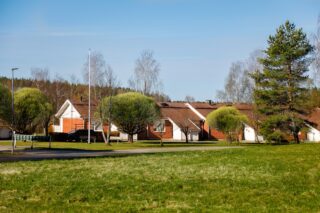 Etualalla vihertävää nurmikkoa, taustalla harjakattoisia, uudekoja asuinrakennuksia.