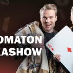 Kaksi nuorta miestä esiintymisvaatteissa. Toisella miehellä on sylissään erittäin iso pelikortti.