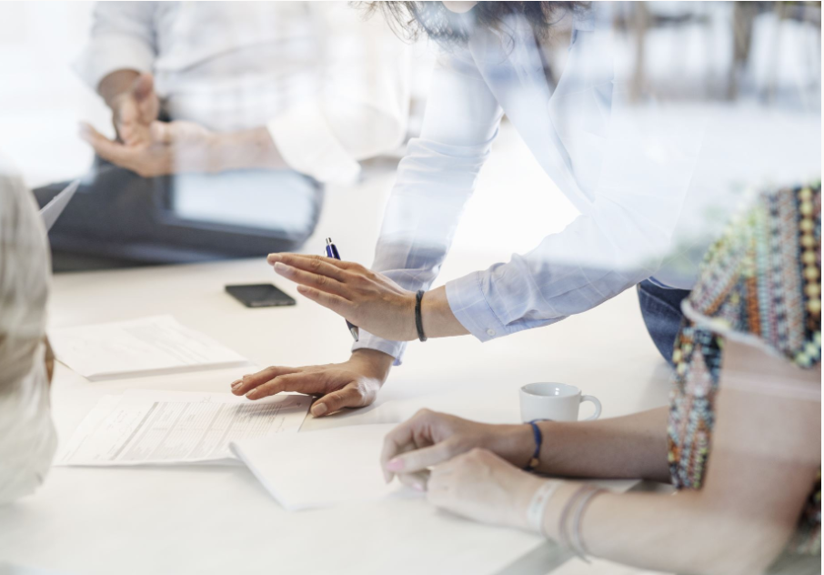 Työpöydän ääressä useampi henkilö, joiden kädet sekä toimistotarvikkeita on näkyvissä.