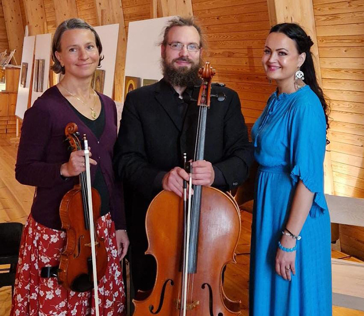 Kaksi naista ja mies seisomassa.. Toisella naisella kädessä viulu ja miehellä sello.