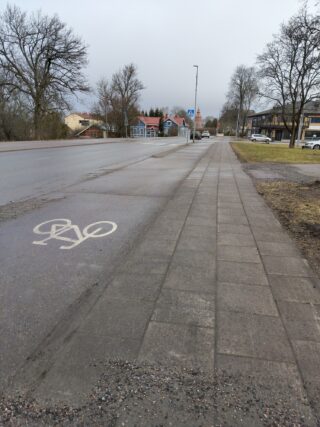 Puhtaaksi harjattu kevyenliikenteen väylä sekä katu. Taustalla näkyy autoja ja etualalla harjaamatointa, hiekkaista kevyenliikenteenväylää.