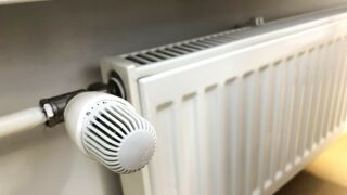 Valkoinen, seinäkiinnitteinen lämmityspatteri. Etualalla termostaatti.