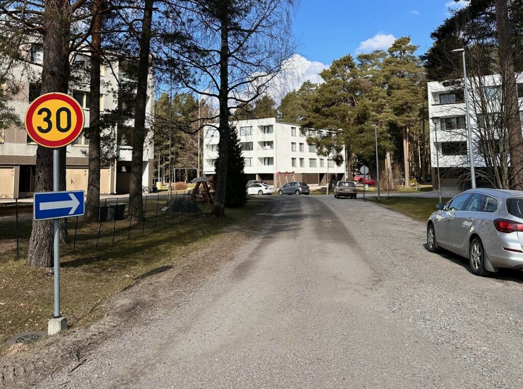 Sorapintainen Mäkiläntie kuvattuna Välitien suunnalta, taustalla valkoisia kerrostaloja.