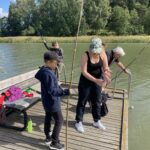 Eri-ikäisiä onkijoita laiturilla kesäisessä, aurinkoisessa säässä.