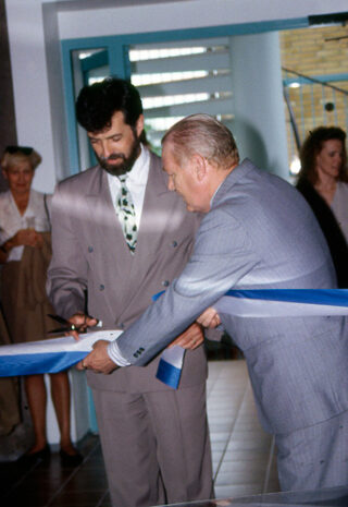 kaksi miestä, joista toinen leikkaa nauhaa saksilla. Taka-alalla kaksi naista.