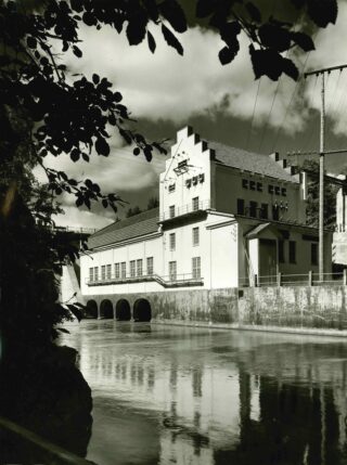 Etualalla puun lehtiä ja vettä, takana voimalaitos ja sähkötolppa