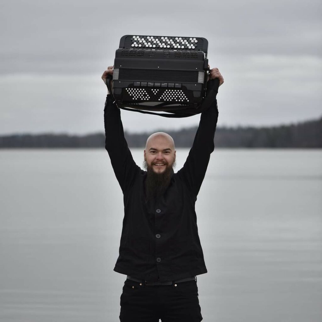 Tummaan asuun pukeutunut mies seisoo rannalla ja pitää päänsä päällä haitaria.