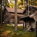 Kaksi vanhaa puurakennusta puiden keskellä