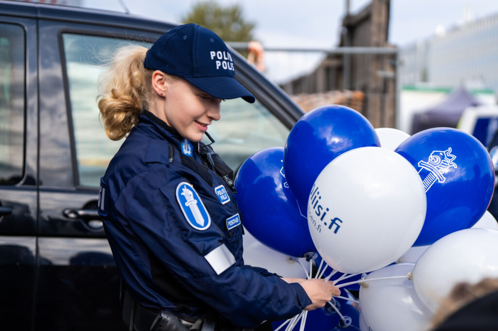 Poliisiasuisella vaaleatukkaisella naisella on käsissään valkoisia ja sinisiä ilmapalloja.