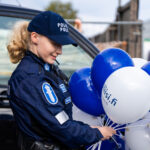 Poliisiasuisella vaaleatukkaisella naisella on käsissään valkoisia ja sinisiä ilmapalloja.