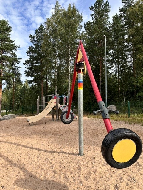 Saaren leikkipaikka, etualalla rengaskaruselli ja takana liukumäki sekä kiipeilyteline.