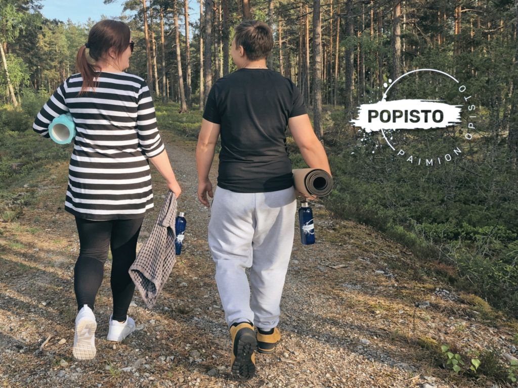 Kaksi henkilöä kävelee metsäpolulla joogamatot ja juomapullot mukanaan