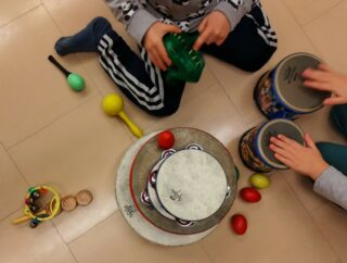 Lapset soittavat muskarissa rumpuja ja muita rytmisoittimia lattialla istuen