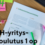 Pöydällä avoinna oleva kirja ja muistiinpanovälineitä sekä päällystettyjä makeisia.