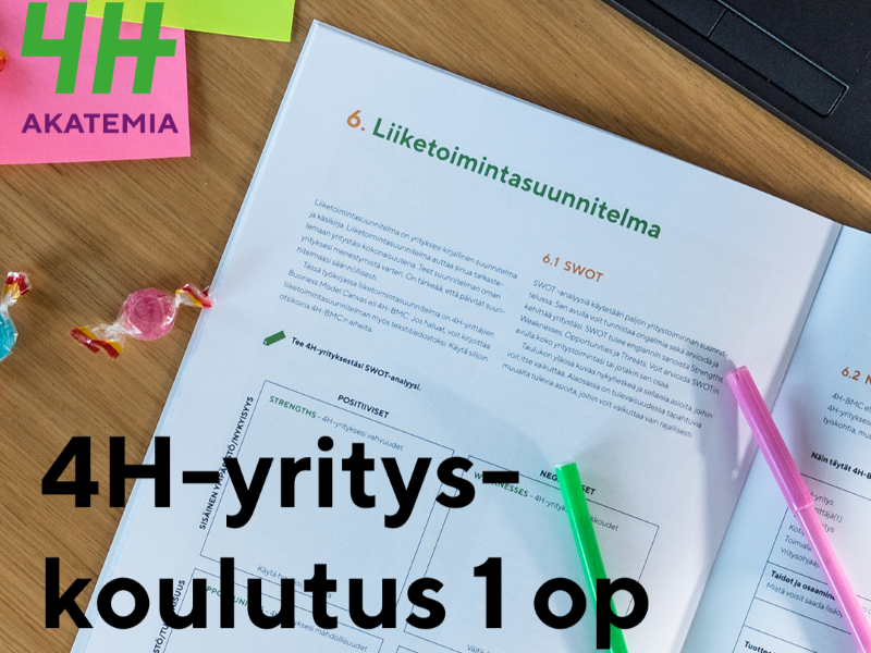Pöydällä avoinna oleva kirja ja muistiinpanovälineitä sekä päällystettyjä makeisia.