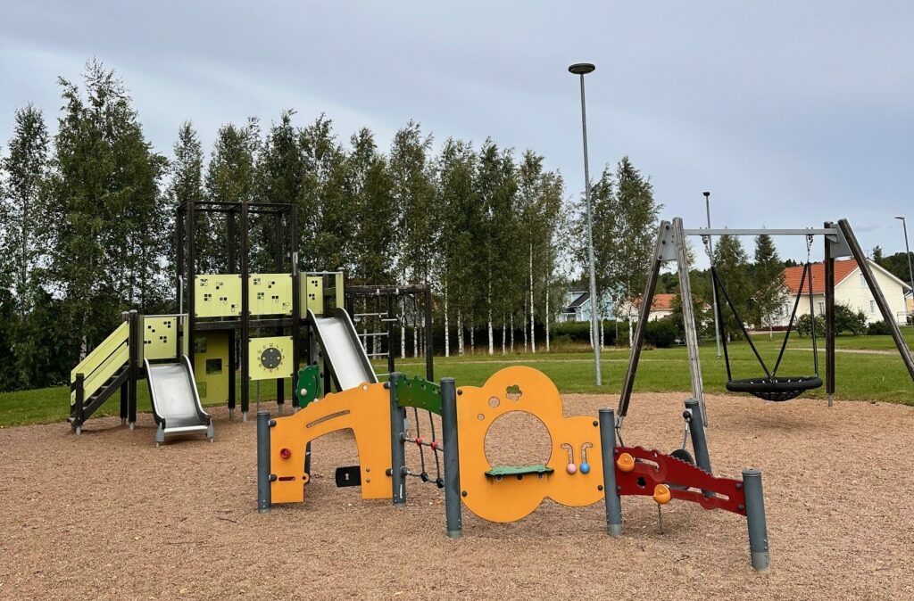 Leikkipuiston kiipeilytelineitä ja hämähäkkikeinu hiekka-alustalla.